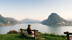 Woman relaxes above lake and mountains on bench